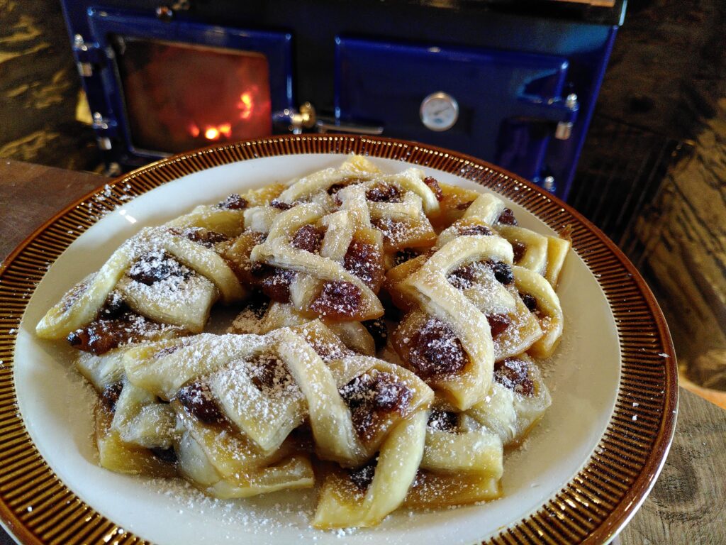 Homemade Christmas pastries - mince twists dusted in icing sugar. Presented on a plate in front of a woodburning range in a farm house kitchen.