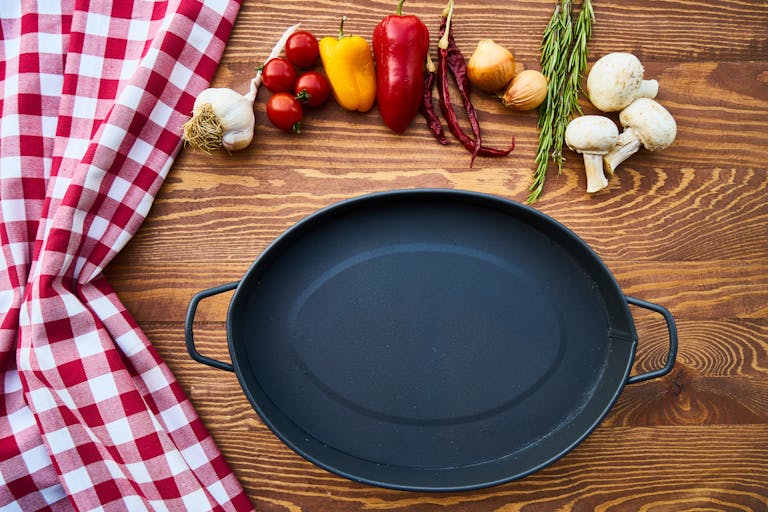 Cast Iron Skillet on Table With a selection of vegetables arranged above it and a red gingham tablecloth to the side.