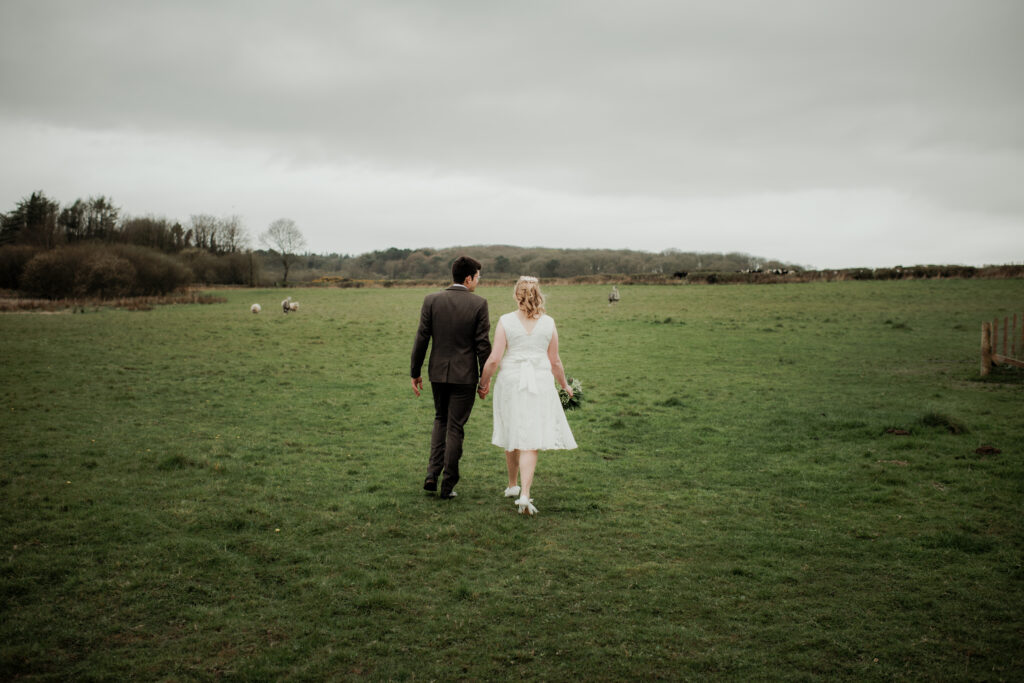 A couple on their wedding day, walking across an open field.