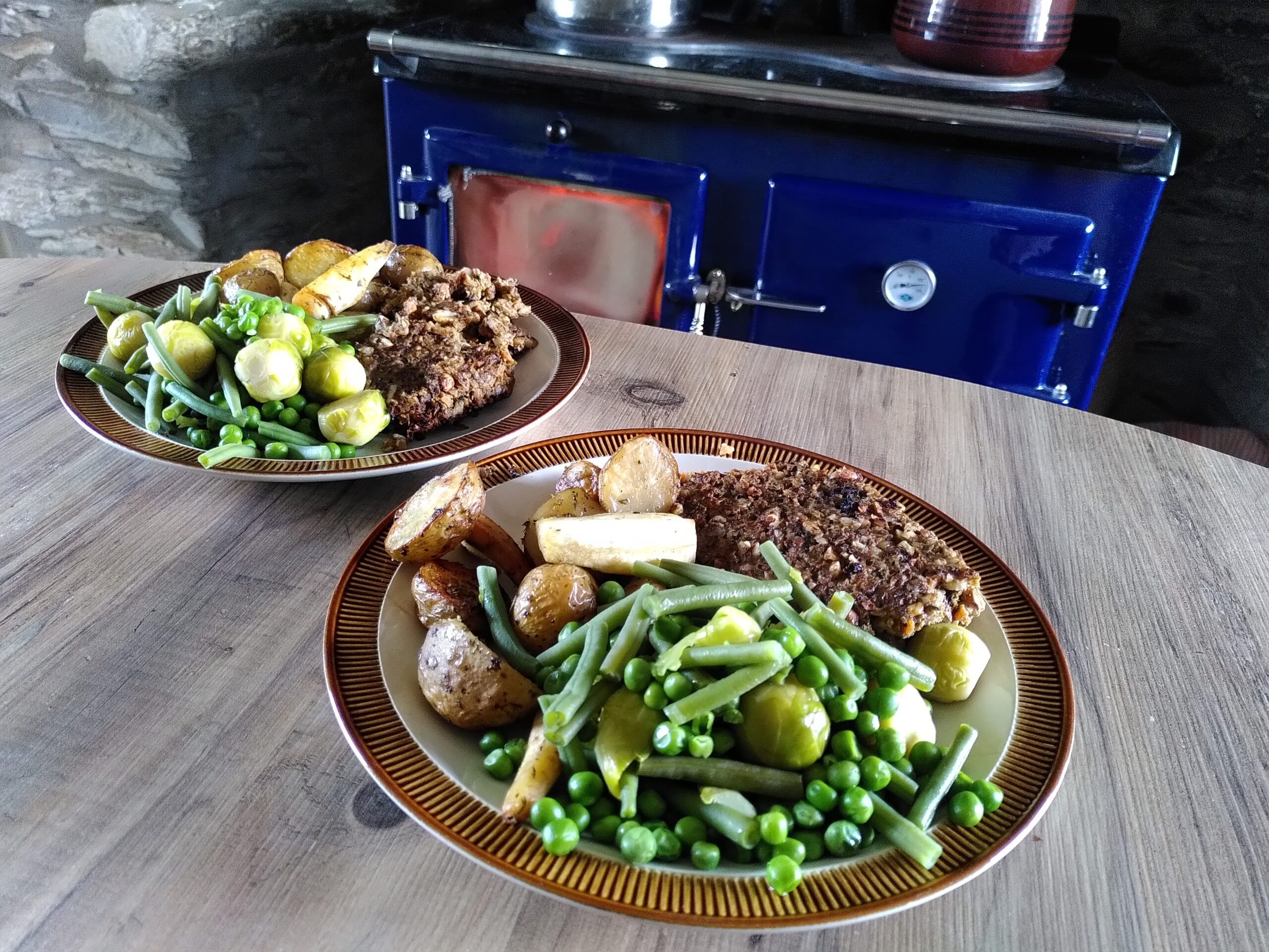 A vegetarian nut roast, served with roast potatoes and seasonal vegetables. There is a wood burning range in the background. Farmhouse kitchen