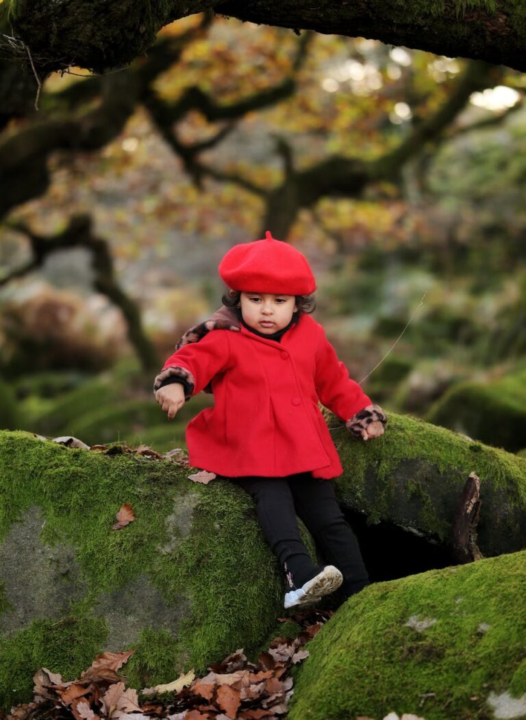 A small child sitting on a log in a forest