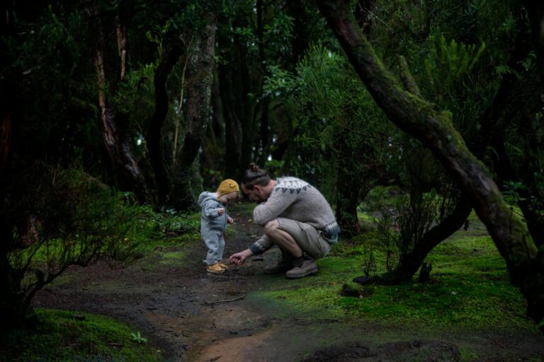 A father and child in a forest. The father is kneeling down to do up this child's shoe.