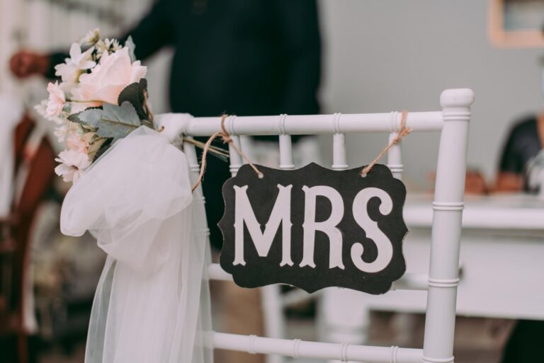 The bride's seat at a wedding reception. A slate sign saying "Mrs" is hung on the back of the chair.