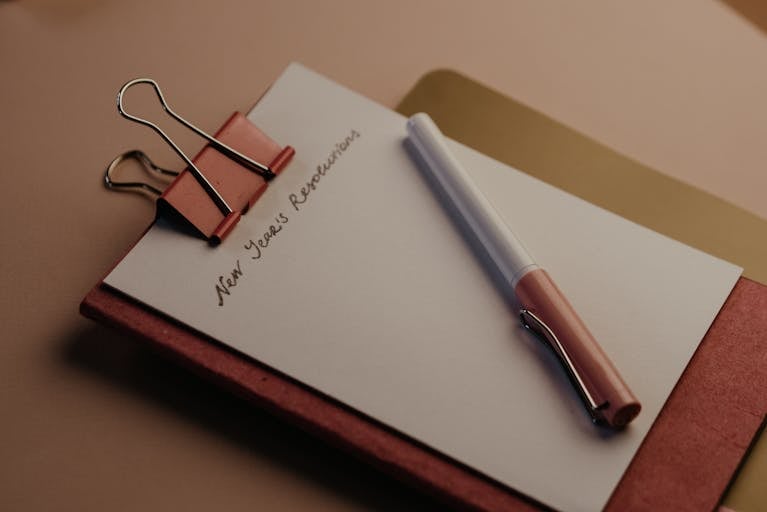 Red Notebook and fountain pen on a desk. The title "New Year's Resolutions" has been written in ink at the top of the page.