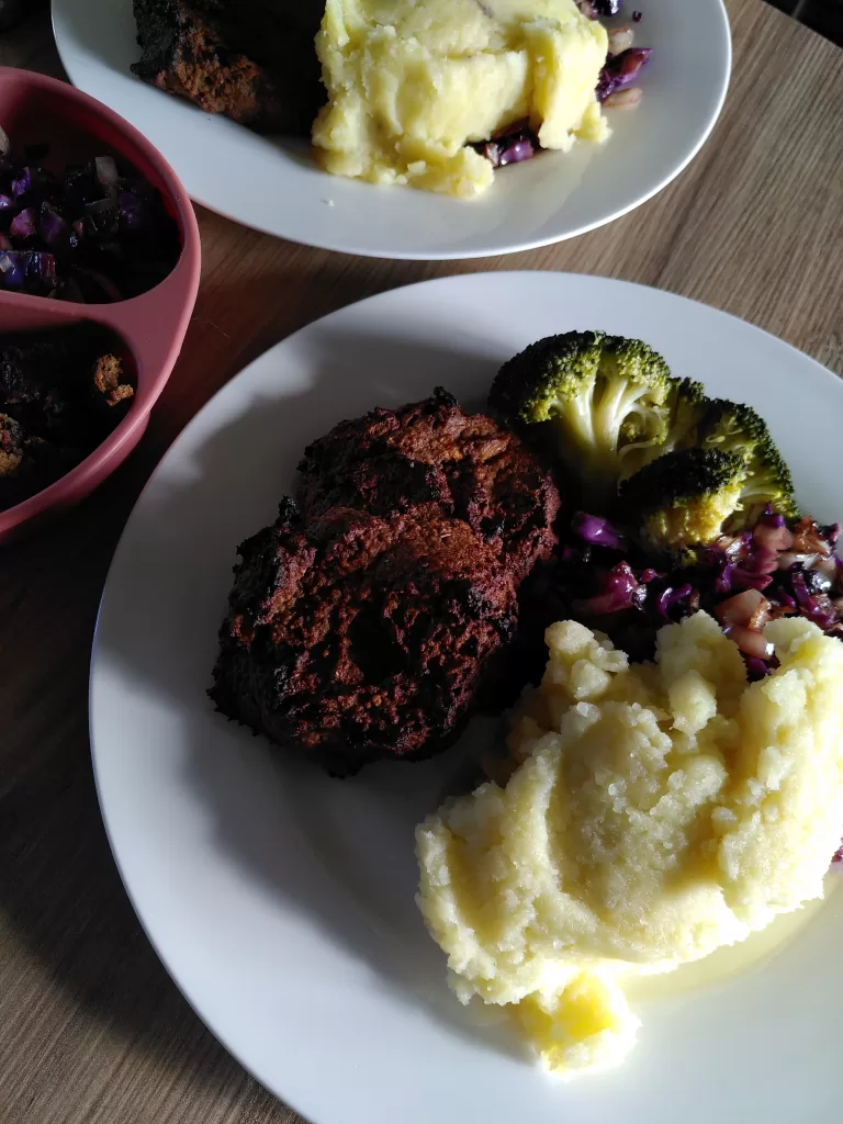 Fruit and nut burgers served with mashed potatoes, steamed broccoli, red cabbage and onion. Pictured in a farmhouse kitchen in front of a wood-burning range,