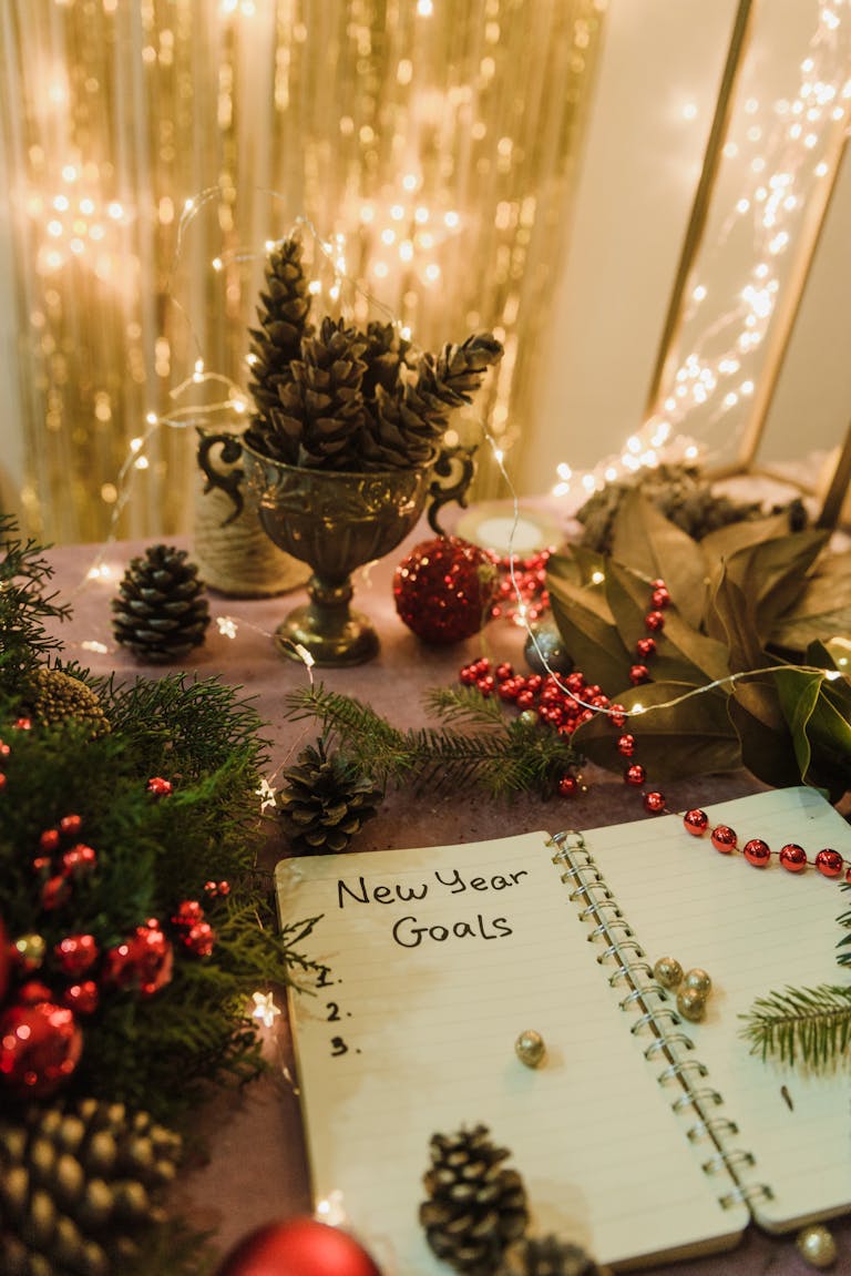 New Year goals written in a notebook surrounded by festive Christmas decorations and twinkling lights.