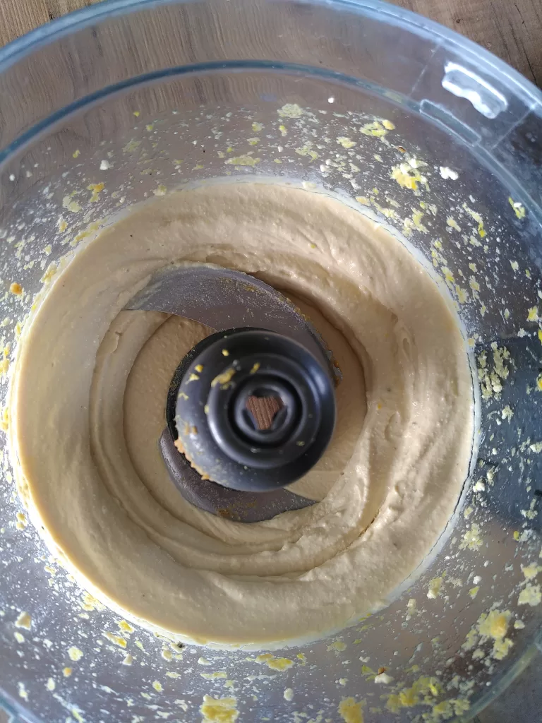 The bowl of a food processor, photographed from above. Inside the bowl is a creamy tofu-based sauce for a vegan fishy pie.